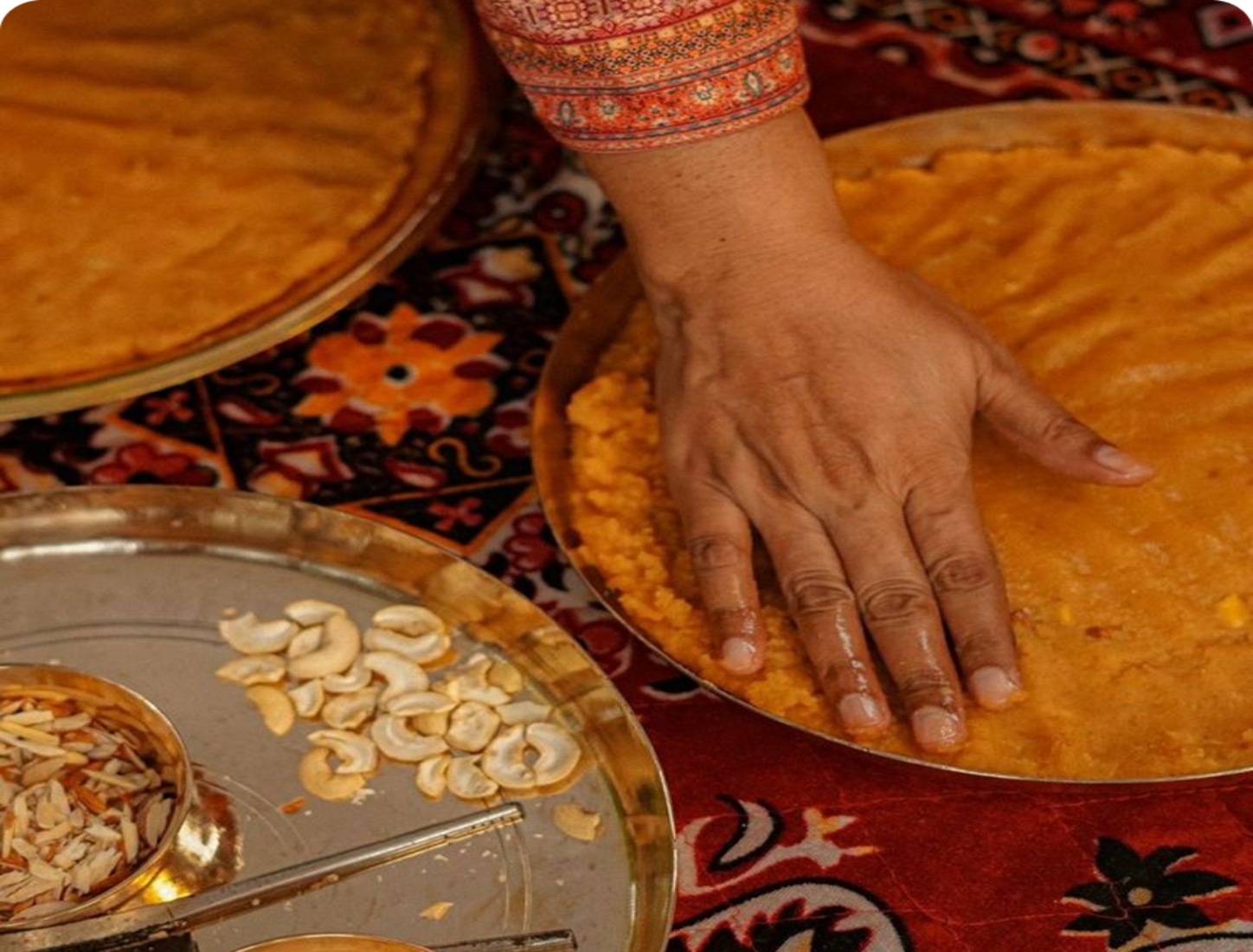 Hand making a flatbread on a traditional patterned surface with spices nearby.